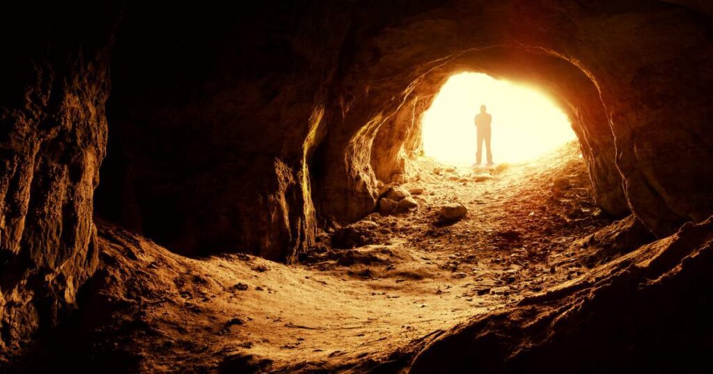 A man standing in a cave of Lascaux with sunlight streaming in from above.