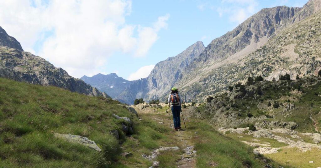 A man hiking in the mountains, surrounded by lush greenery and towering peaks of Pyrenees.