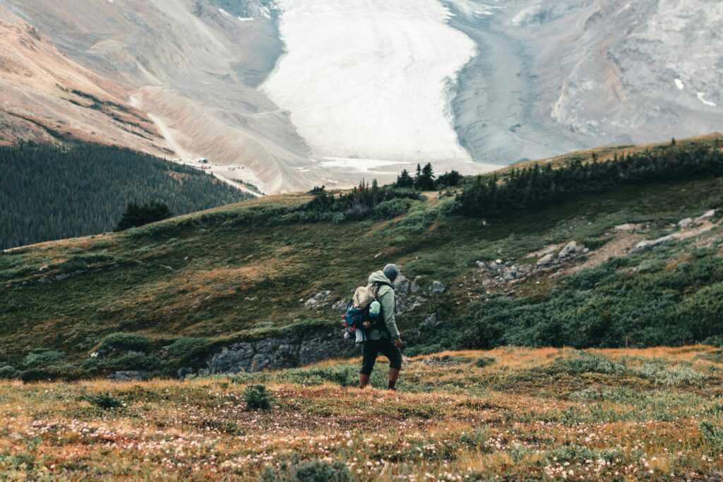 A hiker with a backpack walking through a Canadian field with mountains in the background.